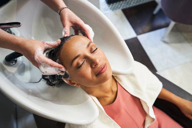 Top view of client sitting close to sink Relaxed international woman closing her eyes while hairdresser washing her hair hair salon photos stock pictures, royalty-free photos & images