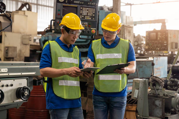 trabajador masculino de la fábrica asiática discutiendo y buscando el documento del portapapeles para el metal del torno de la máquina de mantenimiento en la fábrica de la industria. trabajador de ingeniería que utiliza un documento manual para la má - manual worker portrait helmet technology fotografías e imágenes de stock