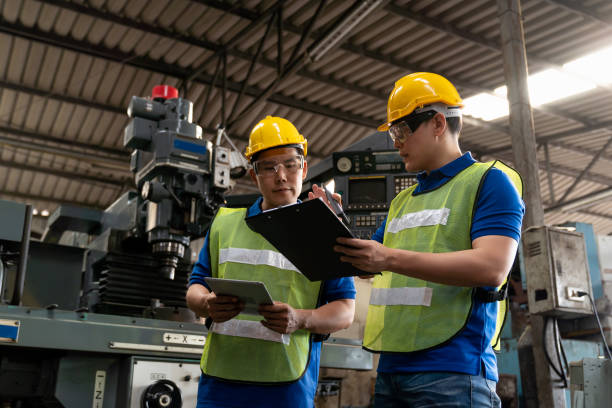 trabajador masculino de la fábrica discutiendo y buscando el documento del portapapeles para el mantenimiento del torno metálico de la máquina en la fábrica de la industria. trabajador de ingeniería que utiliza un documento manual para la máquina de  - manual worker portrait helmet technology fotografías e imágenes de stock