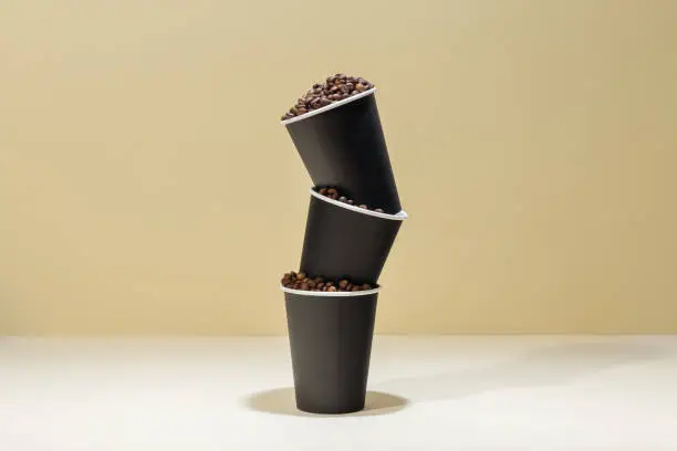 Three black paper coffee cups filled with coffee beans, on a beige background