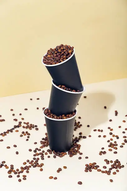 Black paper coffee cups filled with coffee beans, on a beige background