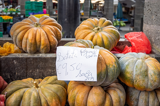 Pumpkins with a handwritten price tag at a market stall at the mercado which is a marketplace under roof in the center of the city with public access. In several market stalls fresh and locally produced food is sold – mostly fruit and vegetables but also fish and meat. The picture is taken in Ponta Delgada at the Azorean Island San Miguel in the middle of the North Atlantic Ocean.