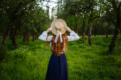 Summer portrait, beautiful freckled young woman wearing straw hat . Girl in the spring apple garden