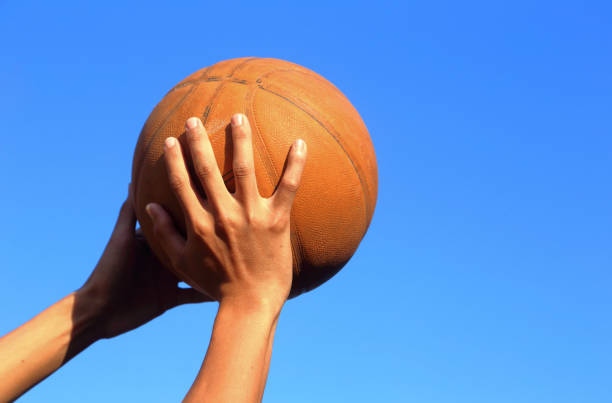 istock Hand shooting basketball on blue sky background 1339288175
