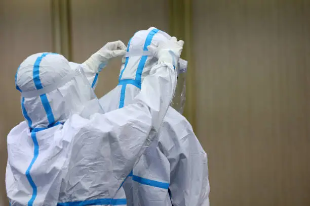 Photo of medical worker in a PPE suit (Personal Protective Equipment) white color with face shield a hard day's work. Take a break to enter a Covid-19 patient's room in the hospital's intensive care unit.