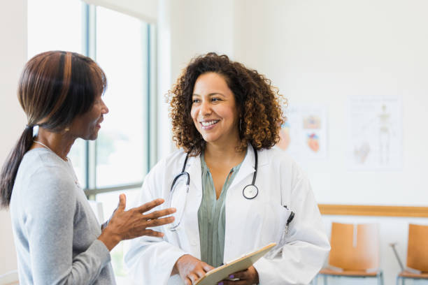 Standing together, female doctor smiles while mature female patient speaks Standing together in the medical clinic, the mid adult female doctor smiles as she listens to the  mature adult female patient. womens issues stock pictures, royalty-free photos & images