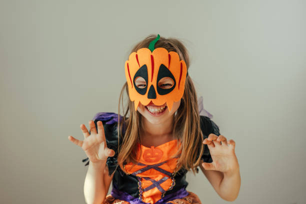 Portrait of little girl dressed Halloween witch costume and pumpkin mask Portrait of little girl dressed Halloween witch costume and pumpkin mask indoor. Selective focus. mask disguise stock pictures, royalty-free photos & images