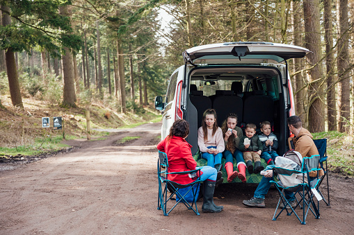 Family on a day out in Thrunton woods together in the North East of England. They are sitting together in the boot of a van eating a picnic/packed lunch.