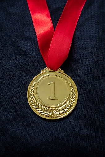 Medal gold, Winner prize award hanging with red color ribbon on athlete chest. Golden trophy in sport for first place champion on black color shirt background