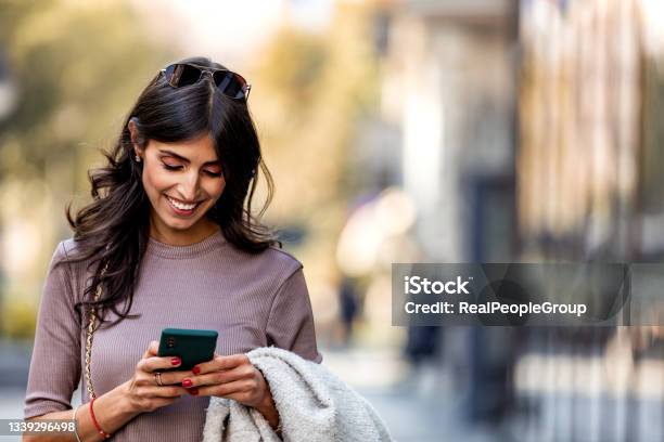 Beautiful Mid Adult Woman Walking And Texting Message On Mobile Phone Outside Business Center Stock Photo - Download Image Now