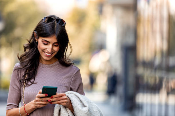 piękna średnio dorosła kobieta chodząca i wysyłająca wiadomości tekstowe na telefon komórkowy przed centrum biznesowym. - mature adult business person meeting caucasian zdjęcia i obrazy z banku zdjęć