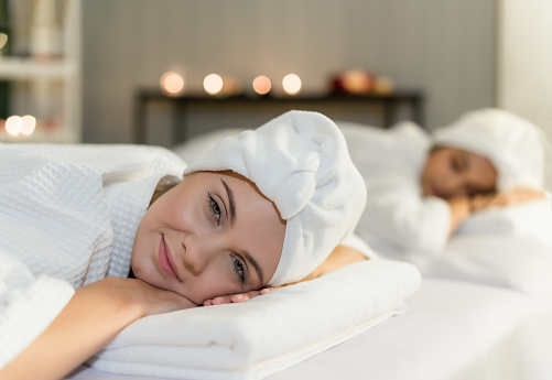 Two young woman friends lying down and relaxing on massage beds preparation for facial treatment and beauty therapy in spa salon. Lifestyle of beautiful women in luxury spa resort. Wellness concept.