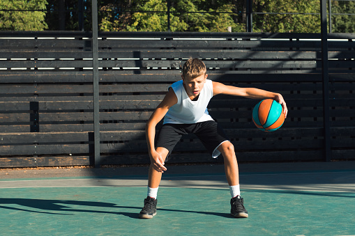 Teenager boy basketball player dribbling on sports ground