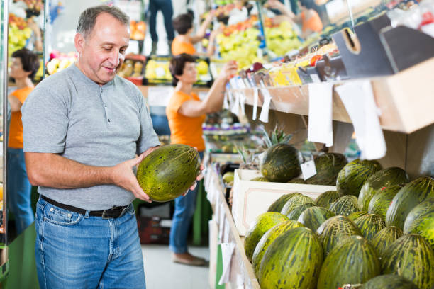 Glad man is choosing ripe melon in the store