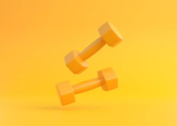 dos mancuernas de fitness recubiertas de goma amarilla o plástico que caen sobre fondo amarillo - barbell exercising sport gym fotografías e imágenes de stock