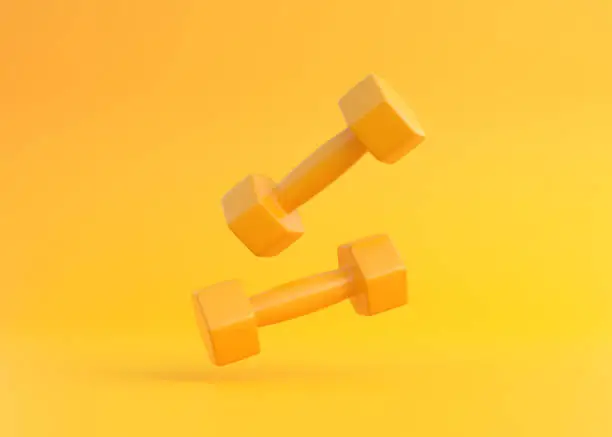 Two yellow rubber or plastic coated fitness dumbbells falling on yellow background. Sport equipment. Minimal creative concept. 3D render illustration
