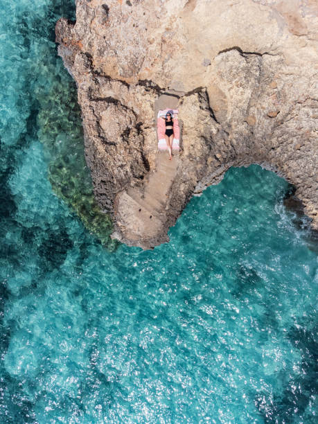 a woman is resting on a rock near a turquoise sea - palma majorca stok fotoğraflar ve resimler