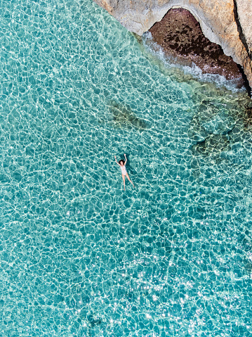 A woman is relaxing in a transparent turquoise sea. Aerial view of a woman lying down in the sea.