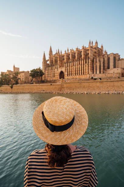 rear view of a woman with a straw hat while she's admiring the cathedral de santa maría de palma de mallorca at sunset - palma majorca stok fotoğraflar ve resimler