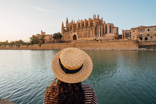 Rear view of a woman with a straw hat while she's admiring the Cathedral de Santa María de Palma de Mallorca at sunset