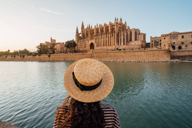 Rear view of a woman with a straw hat while she's admiring the Cathedral de Santa María de Palma de Mallorca at sunset Rear view of a woman with a straw hat while she's admiring the Cathedral de Santa María de Palma de Mallorca at sunset. The Cathedral reflects in the water. majorca photos stock pictures, royalty-free photos & images