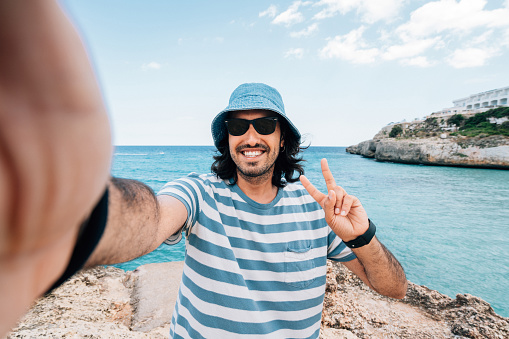 A man is taking a selfie near the sea. He's wearing a bucket hat. Pov view.