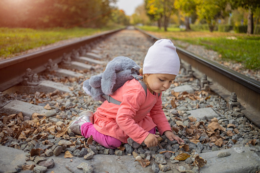 cute toddler girl playing with stones on the railroad embankment. dangerous games