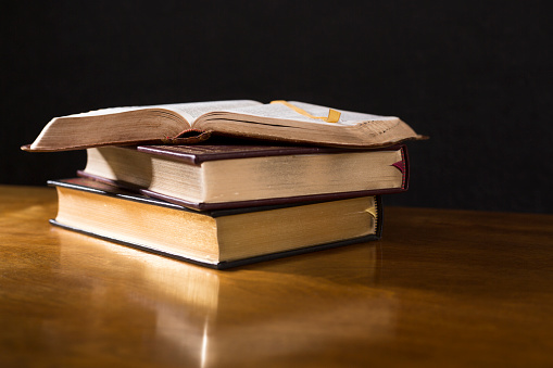 Open  book or Bible on stack of other leather bound books.  Highly polished wood table.  Black background.  Room for copy.