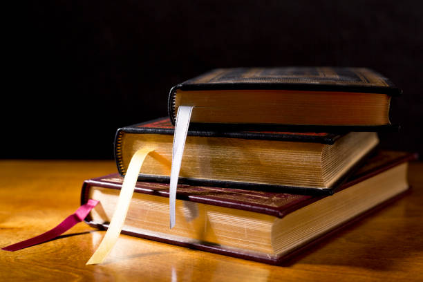 Stack of  beautiful leather bound books.  Highly polished wood table.  Black background.  Satin ribbon bookmarks.  Room for copy.