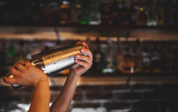femme au bar tient un shaker en acier dans ses mains, le secoue pour faire un cocktail. - shaker photos et images de collection