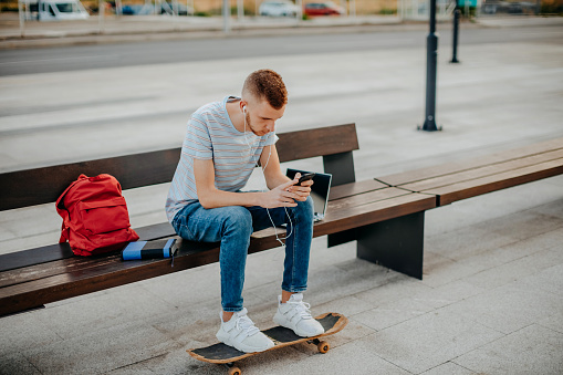 College student sitting outside on bench using mobile phone