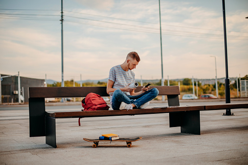 College student sitting outside on bench using mobile phone