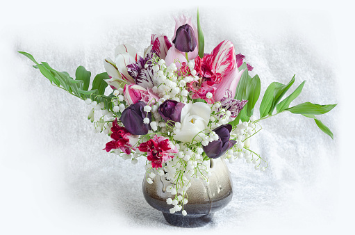 Tulips and lilies of the valley in a ceramic vase, on a light background