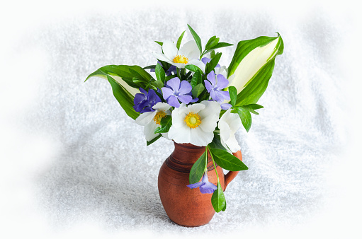 A small bouquet of spring flowers in a clay vase on a light velvet background