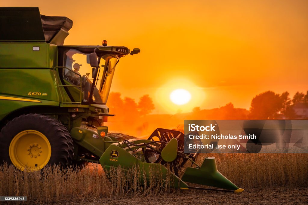 John Deere S670 Soybean Sunset Henry County, Ohio - September 25, 2020: A profile view of a John Deere S670 harvesting soybeans during a hazy sunset with a red and orange sky from the bean dust. Agriculture Stock Photo
