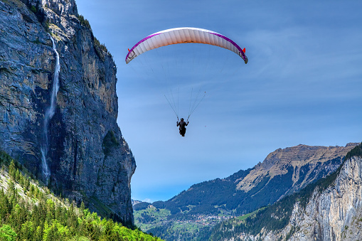 Paraglider fly over mountain slope on a sunny spring day. The sportsman flying on a paraglider. Leisure sports activity in holiday