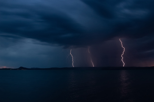 Multiple bright lightning strikes the lake shore during a thunderstorm. Strong electrical storm at night.