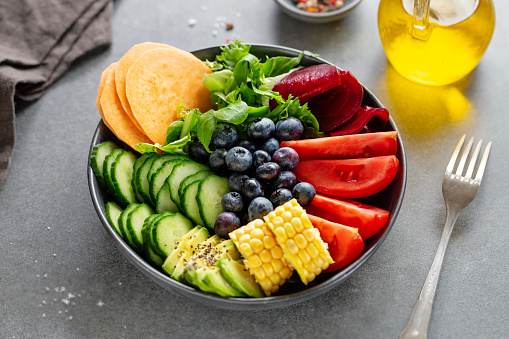 Vegan buddha bowl with vegetables and fruits served in bowl on grey background. Closeup