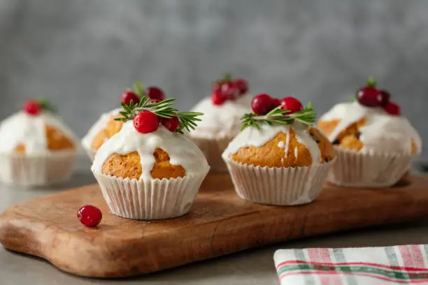 Photo of Christmas muffins with cranberries and rosemary served on wooden board.
