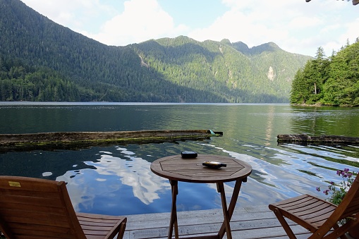 a wood table and two chairs on a deck overlooking the calm scenic ocean with forest and mountains in the background at a remote cabin in Haida Gwaii, British Columbia, Canada