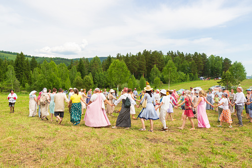 Krasnoyarsk, Russia - June 19, 2021: People holding hands drive a round dance during the celebration of a traditional Slavic holiday of Ivan Kupala. Men and women are dancing around a fire on meadow