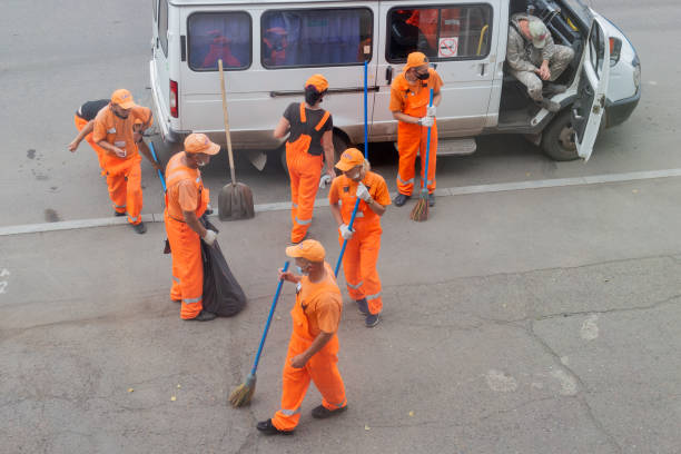 Krasnoyarsk, Russia - 19 August, 2021: Team of janitors in orange uniforms sweeping the street on the road on a summer day