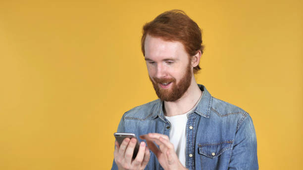 istock Redhead Man Browsing Smartphone Isolated on Yellow Background 1339346951