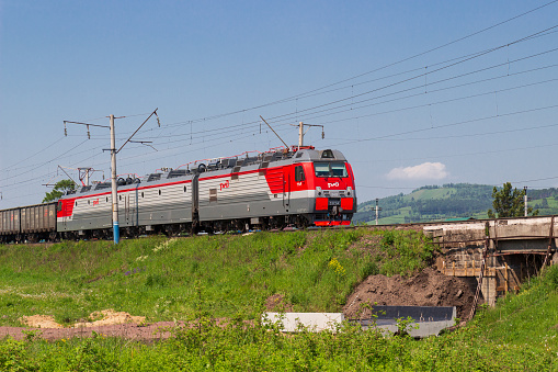 Krasnoyarsk, Russia - June 20, 2021: Red and grey freight train or locomotive with of RZHD logo on Trans-Siberian Railway in summer day in Siberia