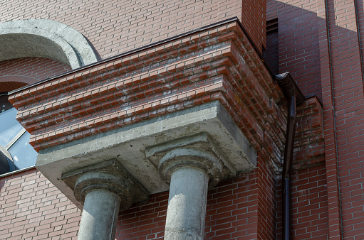 Red brick building with two gray columns. Concrete columns. Drainpipe. Construction Industry. Architecture. View from bottom to top.