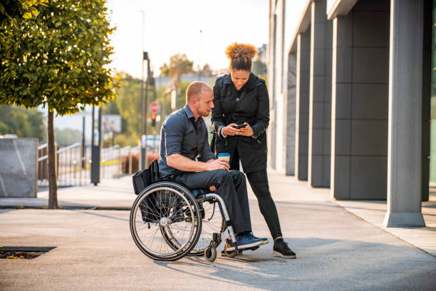 Businessman with physical disability and mixed race businesswoman in their 20s talking and checking smart phone during outdoor coffee break.