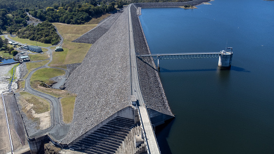Drone view of large scale Australian concrete dam wall and spillway with overhead pedestrian and traffic bridge