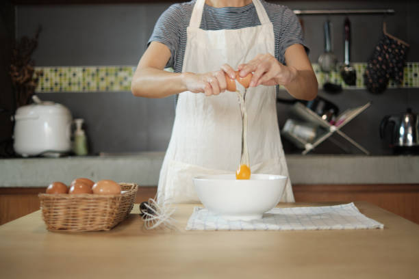 istock Female cook in a white apron is cracking an egg in home's kitchen. 1339379449