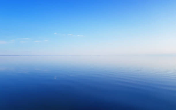 The clear blue sky is reflected in the smooth water surface. Serene summer seascape background with space for copy.