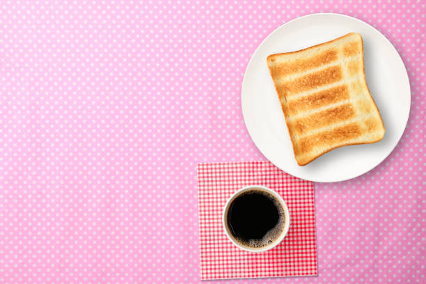 Overhead shot of toasted bread on a white plate with a cup of coffee, on a polka dot tablecloth.